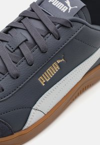 Baskets synthétiques bleu marine avec accents gris, semelle en caoutchouc, zone de lacet texturée et logo doré. Design minimaliste avec une finition lisse.