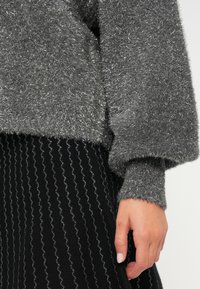 Pelēks, pūkains džemperis ar mīkstu tekstūru un nedaudz spīdīgām šķiedrām. Saskaņots ar melniem svārkiem ar viļņveida sudraba svītru rakstu.