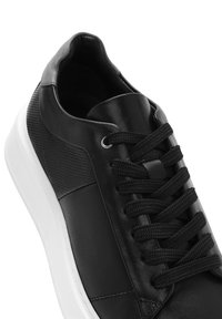 Sneaker nera con dettagli in pelle e texture, punta rotonda, colletto imbottito e design con lacci neri. Suola in gomma bianca per il contrasto.