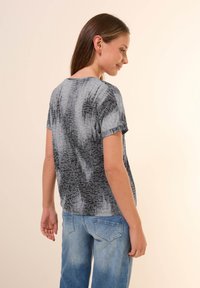T-shirt gris avec un motif texturé comportant des nuances plus claires et plus foncées. Manches courtes et coupe décontractée. Porté avec un jean bleu clair.