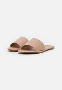 Sandales à talons ouverts en daim rose clair avec un bout ouvert et une large bande sur le devant, dotées d'une semelle plate beige.
