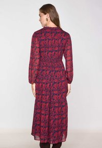 Abito lungo e trasparente con un motivo paisley in rosso e blu navy. Presenta maniche lunghe, vita arricciata e gonna ampia. Chiusura con bottoni al centro della schiena.