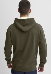 Felpa verde oliva con un grande cappuccio strutturato, polsini a costine e orlo. Tessuto morbido, design minimalista e senza motivi visibili.