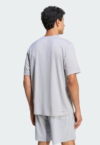 Camiseta gris de manga corta con un corte relajado, textura suave y cuello redondo, combinada con pantalones cortos gris claro que presentan un diseño perforado.