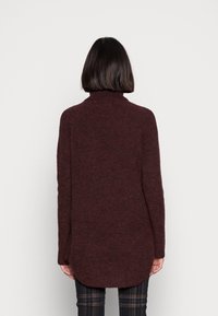 Jersey de cuello alto color burdeos con un ajuste relajado, que presenta un dobladillo redondeado. Mangas largas y una textura suave que realzan el diseño general.