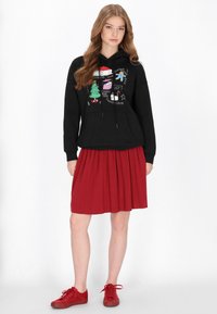 Sudadera negra con capucha y estampado gráfico con símbolos navideños. Combinada con falda plisada roja y zapatillas rojas.