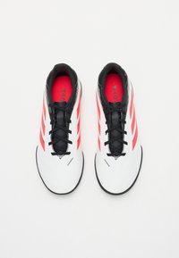 Weißes Sport Schuhwerk mit schwarzen Akzenten, ausgestattet mit drei roten Streifen, einem schlanken Design, strukturierten Oberflächen und schwarzen Schnürsenkeln. Die Innenauskleidung ist rot.