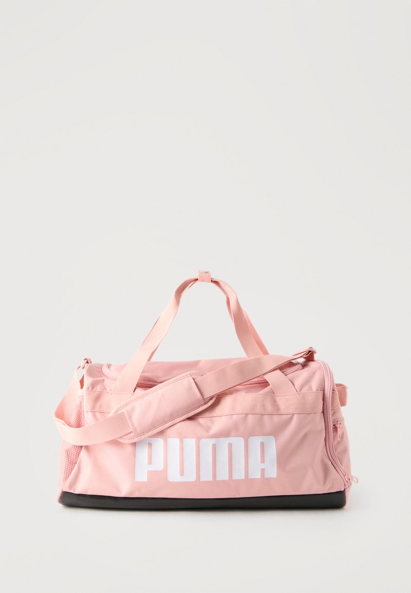 Ροζ αθλητική τσάντα PUMA με λευκό λογότυπο, επάνω λαβές, ιμάντα ώμου, πλαϊνή τσέπη με φερμουάρ και μαύρη βάση σε απλό φόντο.