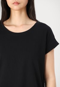 T-shirt en coton noir avec un col rond et des manches courtes roulées. Texture douce, design décontracté, avec une coupe ample.