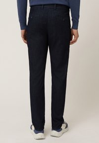 Chinos azul oscuro de tela twill, con dos bolsillos traseros con botones, corte recto, combinados con zapatillas blancas y azules.