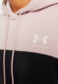 Sudadera con capucha en rosa claro y negro, con una textura suave, cordones y un logo blanco de Under Armour en el pecho.