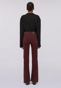 Černý top s dlouhým rukávem v kombinaci s vínovými rozšířenými kalhotami. Kalhoty mají pět kapes a hladkou texturu materiálu. Minimalistický design, elegantní silueta.