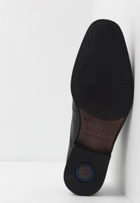 Suola di scarpa in pelle nera con un esterno in gomma testurizzata, che presenta il marchio "bugatti" impresso e un logo circolare blu.