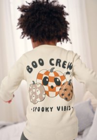 Hellfarbiges Langarmhemd mit einer cartoonhaften Grafik von Kürbissen und dem Text "BOO CREW" und "SPOOKY VIBES". Strukturierter Baumwollstoff.