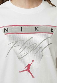 Bílá košile s červeným a šedým logem Nike Flight, s vertikálně pruhovaným trojúhelníkovým designem a červenou siluetou hráče basketbalu.