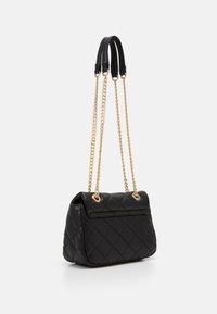 Sac à main matelassé noir avec des anses en cuir et des chaînes dorées. Présente une forme rectangulaire et une poche avant. Texture lisse.