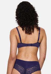 Laivastonsininen alusvaatesetti, joka sisältää pitsiselkäisen tangat ja rintaliivit, joissa on säädettävät olkaimet ja hakasuljent. Setti korostaa sileää pintaa ja yksityiskohtaisia koristeita.