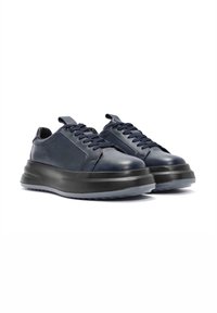 Zapatillas de cuero en un azul marino oscuro con un acabado texturizado, punta redondeada y una suela negra gruesa. Presenta cordones en un tono similar y un diseño minimalista.