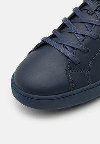 Navy Leder Sneaker mit abgerundetem Zeh, strukturierten Oberflächen und passenden Schnürsenkeln. Die Sohle hat einen kontrastierenden dunkelblauen Rand.