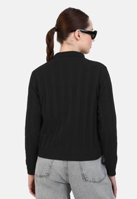 Cardigan nero a coste con colletto strutturato, maniche lunghe e vita aderente, abbinato a jeans in denim grigio chiaro.