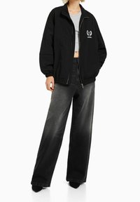 Mustapommitakki, jossa on elastiset hihansuut, hopea vetoketju ja brodeerattu logo. Yhdistetty leveälahkeisiin, haalistuneisiin mustiin farkkuihin.