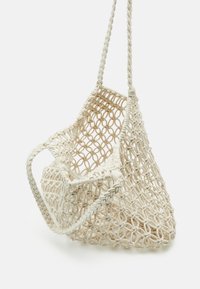 Tkaná macramé taška v neutrální krémové barvě, s složitým kruhovým vzorem, trojúhelníkovým tvarem a zapletenými ramenními popruhy.