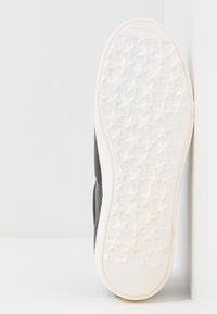 Baskets noires avec une semelle en caoutchouc texturée aux motifs d'étoiles, empeigne en cuir lisse et intermédiaire blanc contrastant.