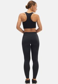 Top corto atlético negro y leggings de cintura alta, ambos en un material liso y elástico, vistos desde la parte posterior. Las zapatillas son negras con suelas blancas.