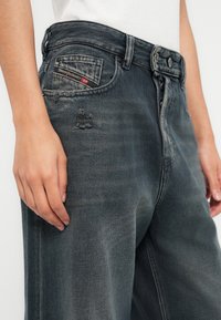Γκρι τζιν denim με άνετη γραμμή, φθαρμένη υφή, κεντημένο λογότυπο στην πίσω τσέπη και αντίθετες ραφές.