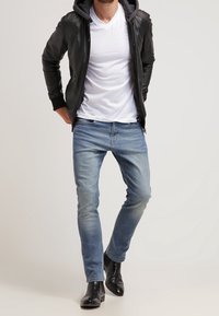 Černá kožená bunda s kapucí, bílé tričko s výstřihem do V, světle modré džíny a černé kotníkové boty. Neformální outfit s přiléhavou siluetou.