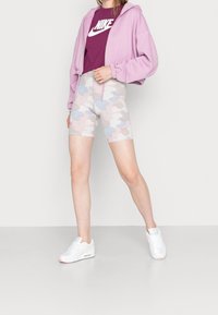 Ljuslila croppad hoodie över en vinröd Nike-t-shirt, ihopparad med pastellfärgad kamouflage cykelshorts och vita sneakers med rosa detaljer.