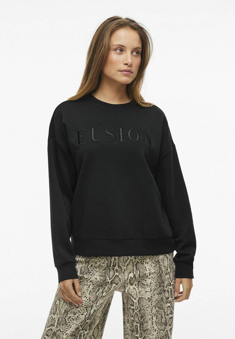 Sudadera negra con texto en relieve "FUSIÓN", cuello redondeado y mangas largas, combinada con pantalones de pierna ancha de estampado de serpiente.