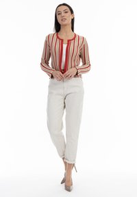 Randig stickad cardigan i beige, röd och brun, med rund hals och åtsittande ärmar. Kombinerad med off-white tapered byxor och beige klackar.