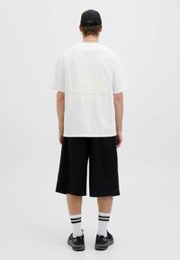 Hvid kortærmet t-shirt med et stort gult solgrafik og "ReelBreak" tekst på ryggen, parret med sorte knælange shorts.