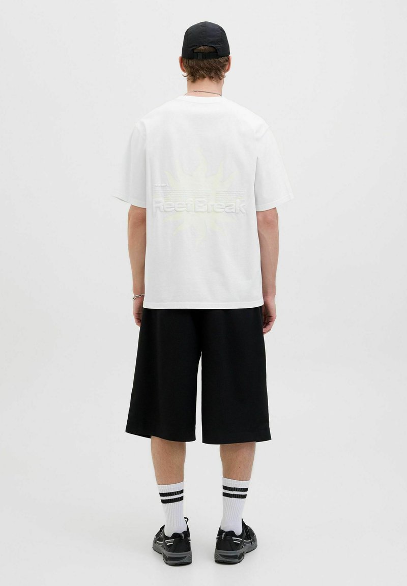Hvid kortærmet t-shirt med et stort gult solgrafik og "ReelBreak" tekst på ryggen, parret med sorte knælange shorts.