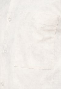 Κοντινό πλάνο ενός λευκού πουκαμίσου με καθαρές ραφές και τετράγωνη τσέπη στο δεξί μέρος.