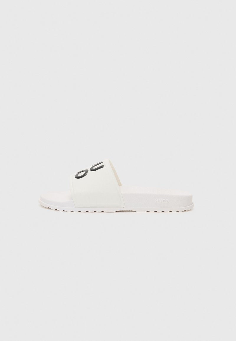 Witte slipper met een gestructureerde band met zwarte letters. De zool is plat en heeft een zigzagpatroon voor grip. Lichtgewicht ontwerp.