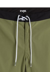 Olijf groene zwembroek met een zwarte tailleband, witte trekkoord en schaakborddetail op de uiteinden. Gemaakt van glad, lichtgewicht materiaal.