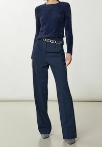 Pull en laine moelleux bleu marine associé à un pantalon taille haute nervuré bleu marine et une ceinture en chaîne argentée. Tissu texturé et silhouette élégante et cintrée.