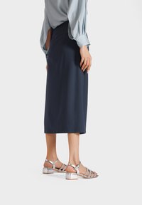 Gonna midi blu marina abbinata a una blusa azzurra chiara. Sandali argentati con tacco a blocco. Tessuto liscio e vestibilità strutturata.