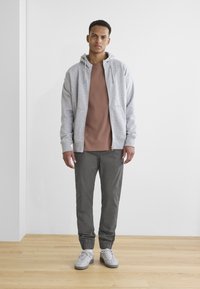 Gray zip-up hoodie over a brown shirt, paired with gray tapered pants and white sneakers. Simple design with soft materials.