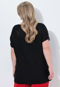 Černý top s krátkým rukávem, volného střihu a zaobleným lemem. Vyrobeno z lehkého materiálu s mírně průhledným detailem na zadní straně.