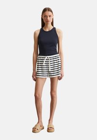 Navy tanktop gecombineerd met witte en navy gestreepte shorts, met een trekkoord in de taille. Model draagt beige textuur slide sandalen.