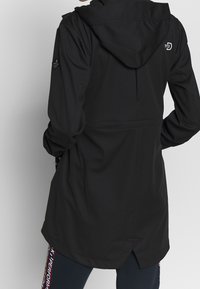 Černá vodotěsná bunda s kapucí, dlouhými rukávy a staženým pasem. Má boční kapsy a logo na horní části zad.