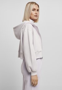Kuttet, zip-up hettegenser i lys lavendel-stoff med stram midje, overdimensjonerte ermer og hette. Kombinert med matchende lys lavendel-bunn.