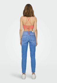 Top cropped in corallo con spalline incrociate abbinato a jeans in denim blu a vita alta. Modella indossa sneakers bianche.