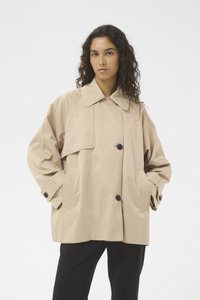Bézs színű ballonkabát széles gallérral, gombos elülső résszel és nagy zsebekkel. Laza szabású, texturált anyagból készült a puhaság érdekében.