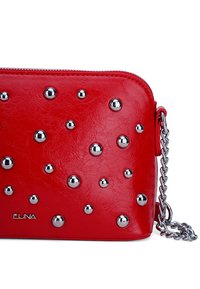 Bolso cruzado de imitación cuero rojo con tachuelas plateadas y una correa de cadena. Superficie texturizada y cierre de cremallera con un pequeño detalle de logo.