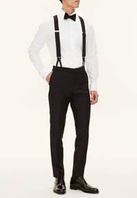 Schwarze formelle Hosen mit Hosenträgern, kombiniert mit einem weißen plissierten Hemd und einer schwarzen Fliege, abgerundet mit polierten schwarzen Schuhen.