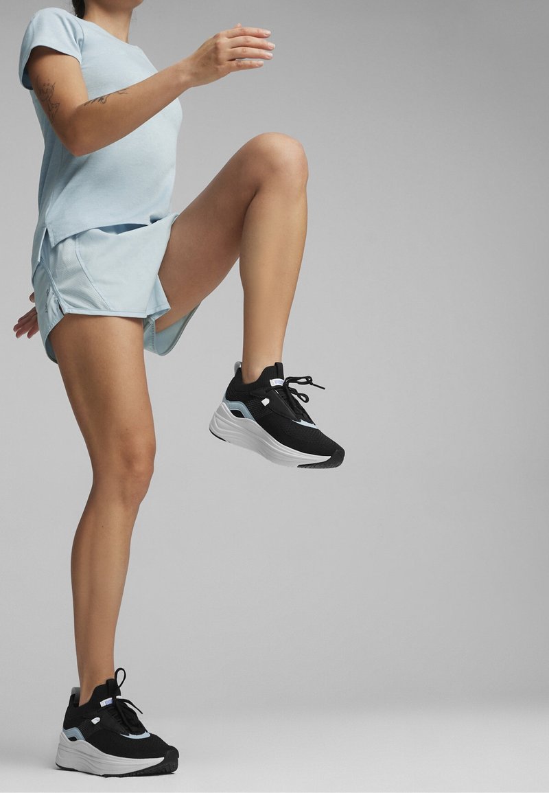 Svartvita atletiska skor med en tjock sula. Ljusblå, kortärmad tröja och matchande shorts. Släta texturer och atletisk passform.